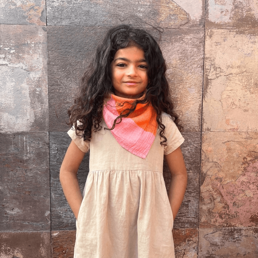 Young girl wearing a colorful small square golden indra limited edition design and beige dress against a textured wall.