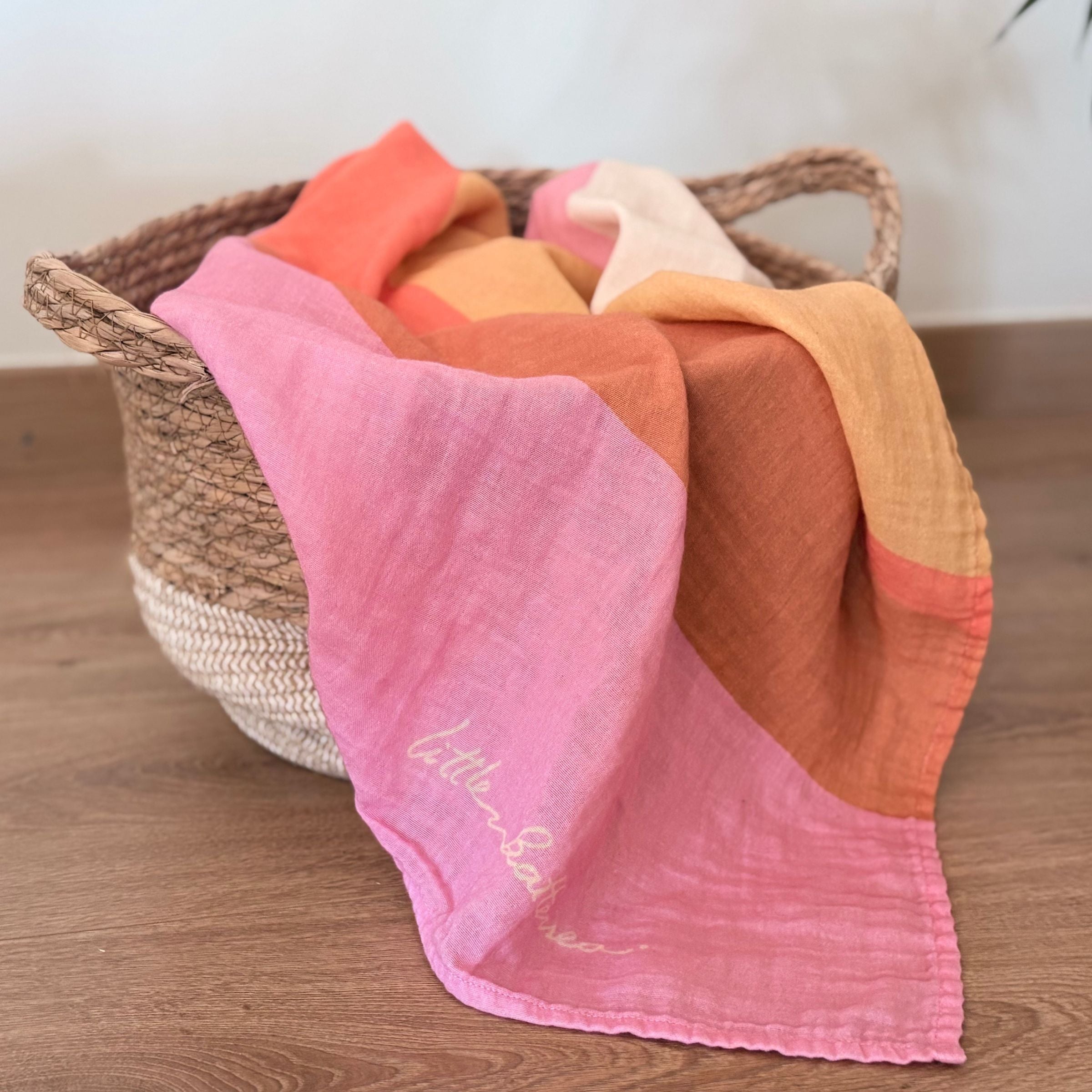 The Large Square Indra with pink and orange hues draped over a woven basket on a wooden surface.