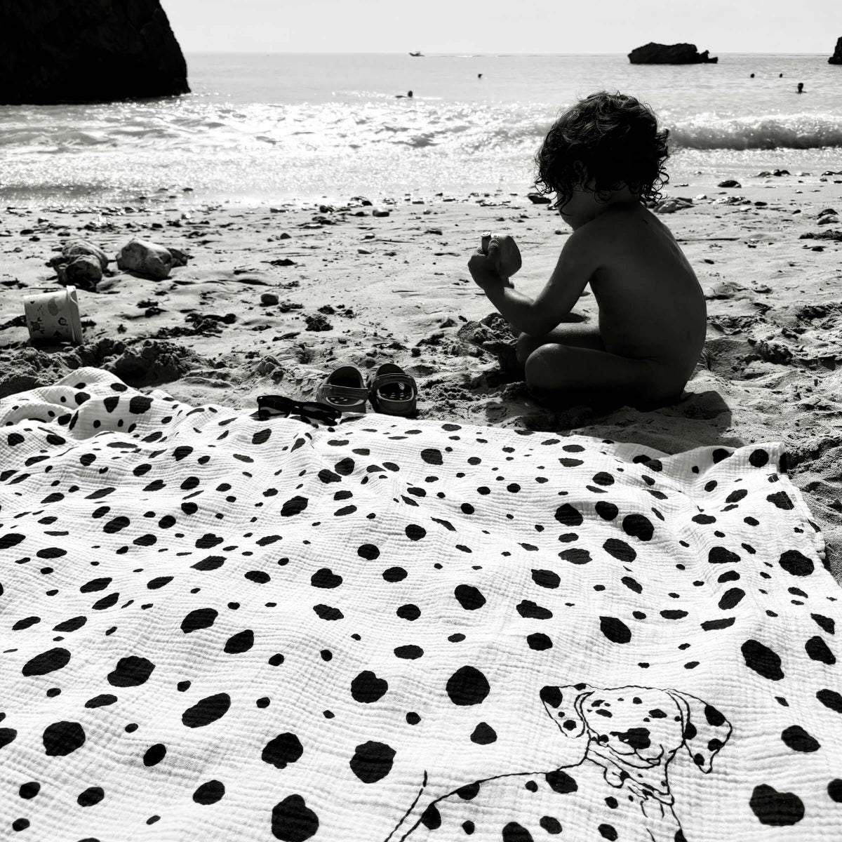 Child playing on a beach with a Dalmatian Allure en Noir Large Square Muslin Blanket