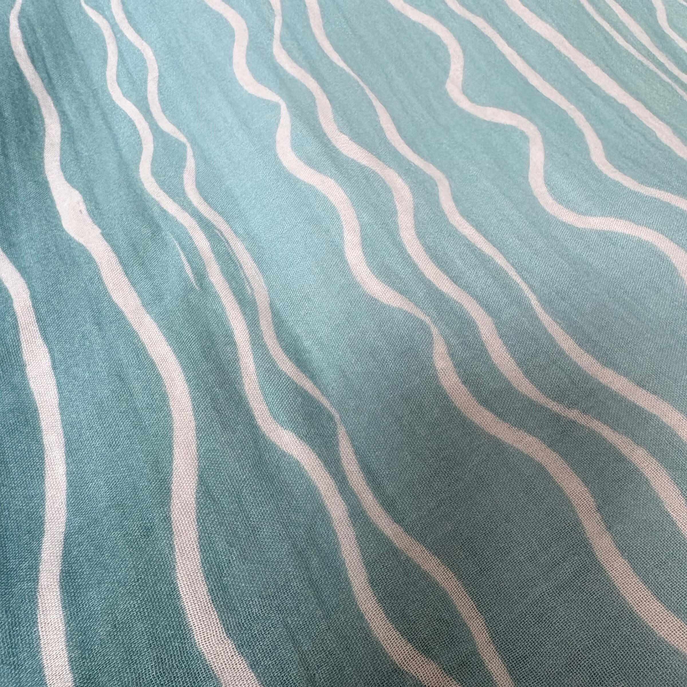 Close‑up view of the Brisa do Mar Small Square muslin fabric, highlighting breathable cotton weave and flowing wave pattern.