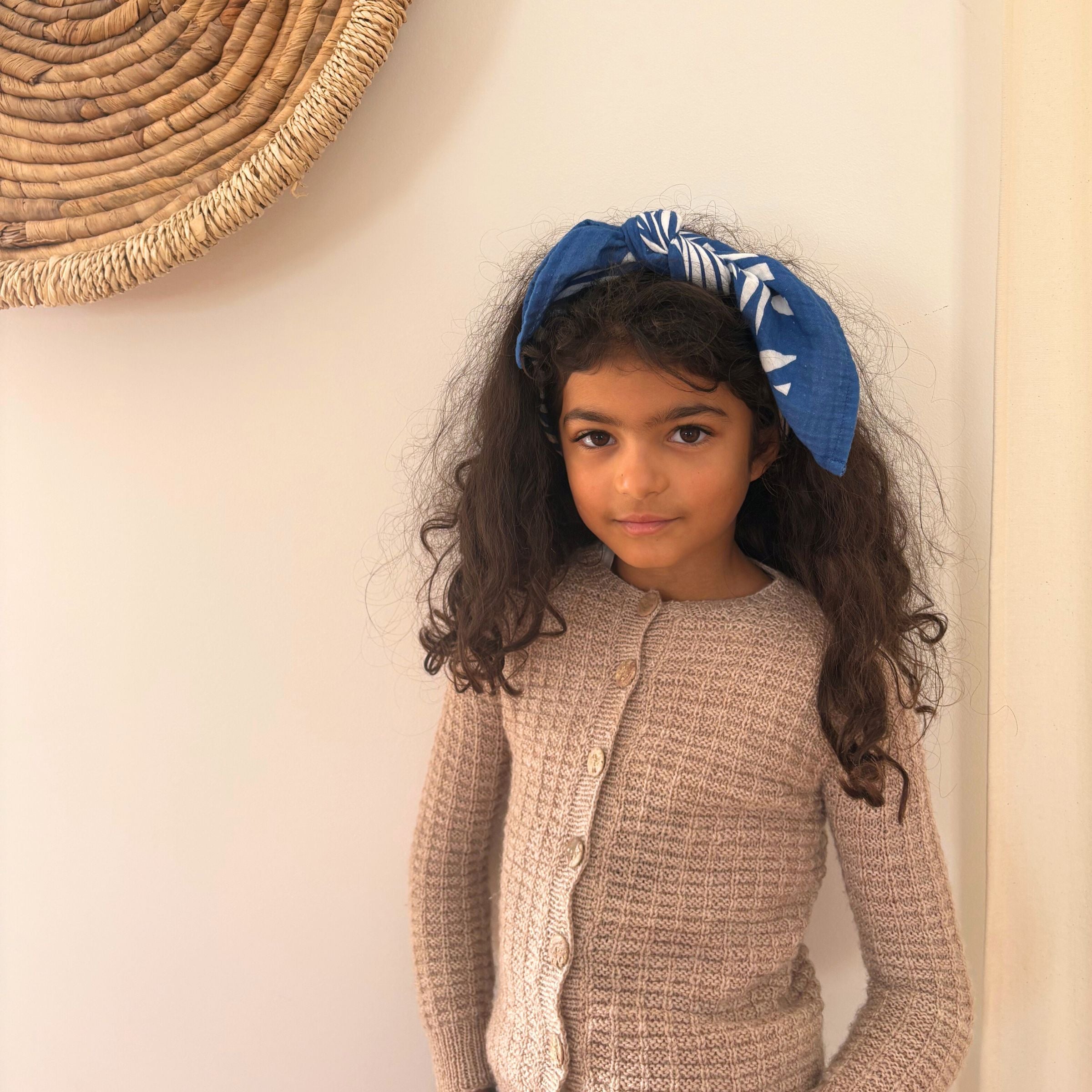 A girl wearing the Azul tropique Small Square muslin as a head scarf bandana, demonstrating continued use as the child grows.