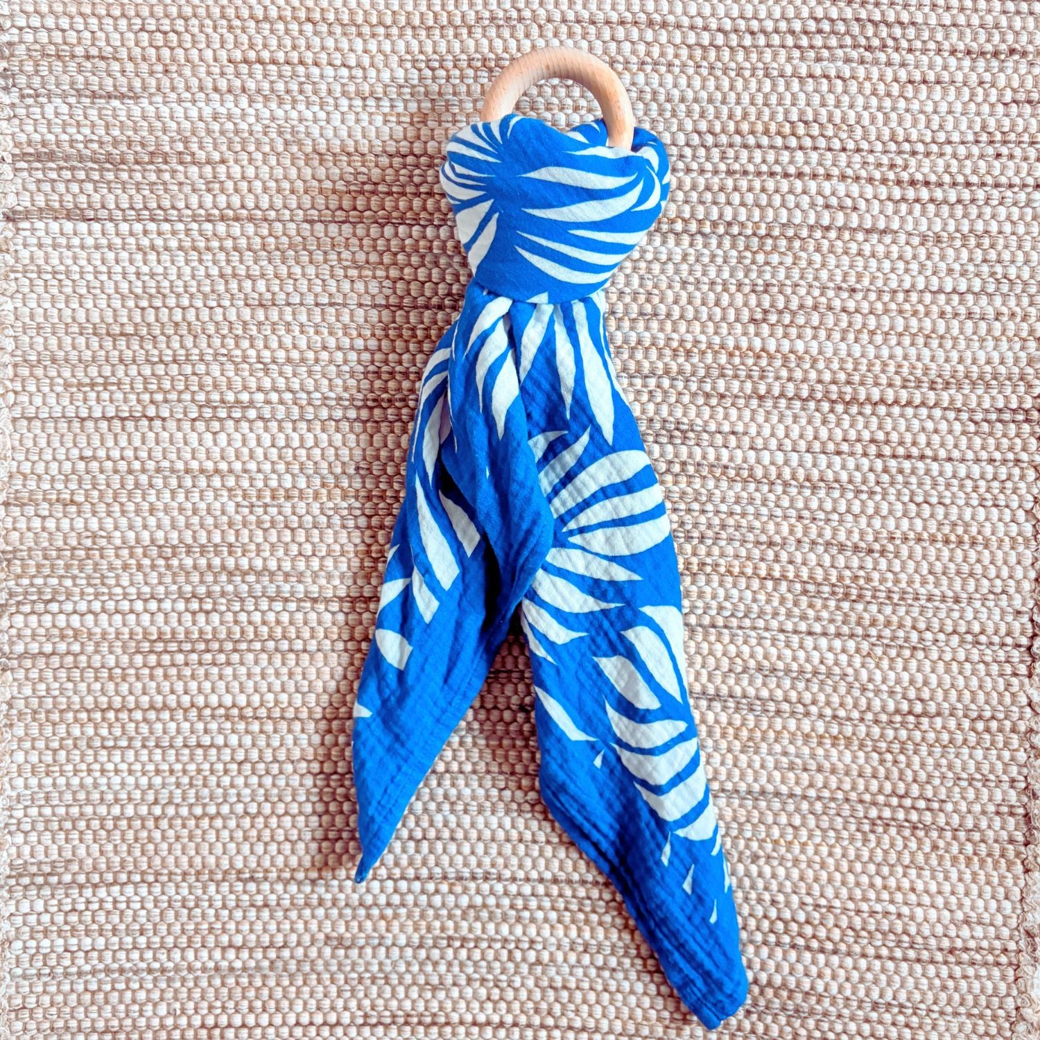 The Small Square muslin tied in a knot around a baby teether, demonstrating versatility beyond swaddling, its also great for play.