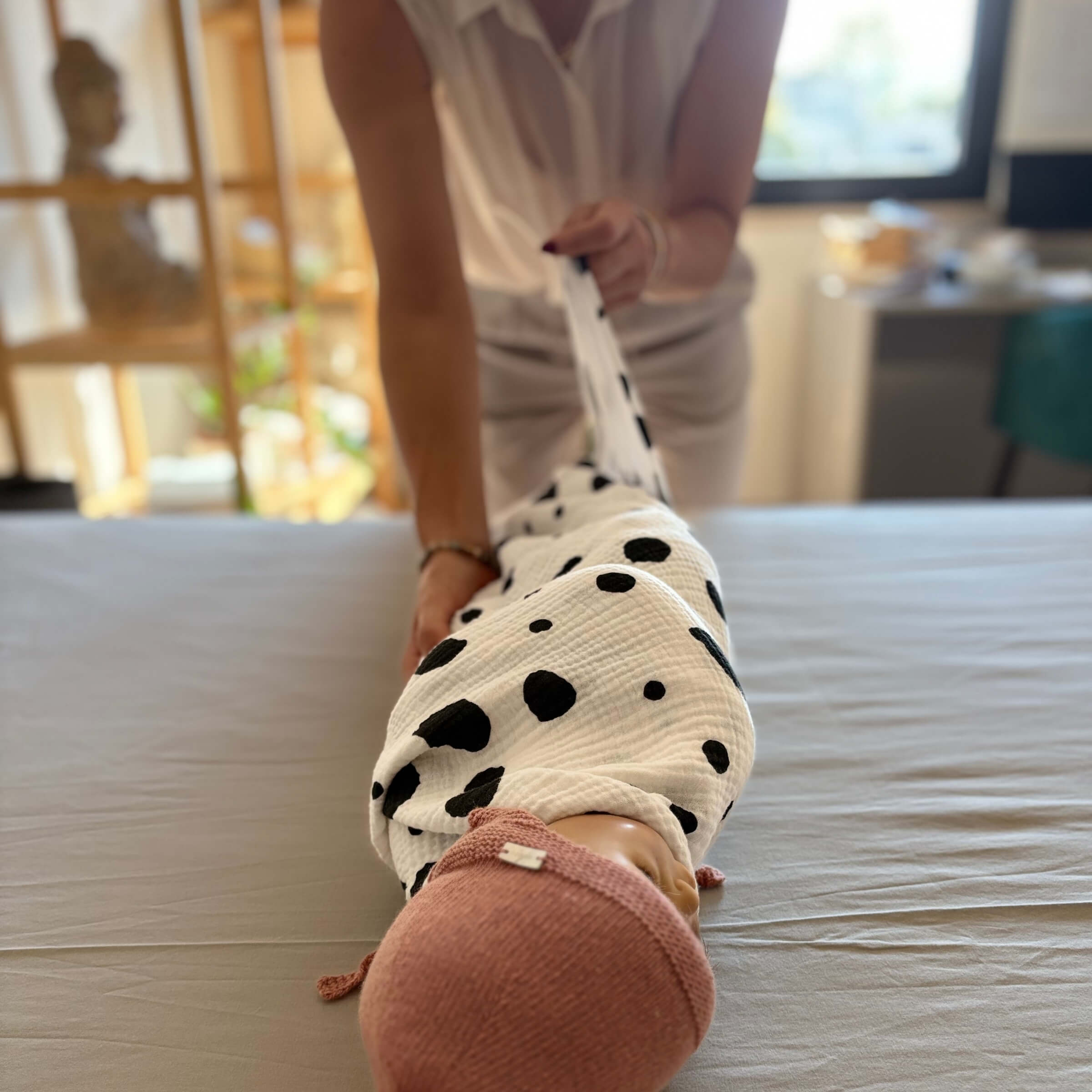 The Small Square muslin wrapped gently around a newborn on a bed, showing softness and scale for early use.
