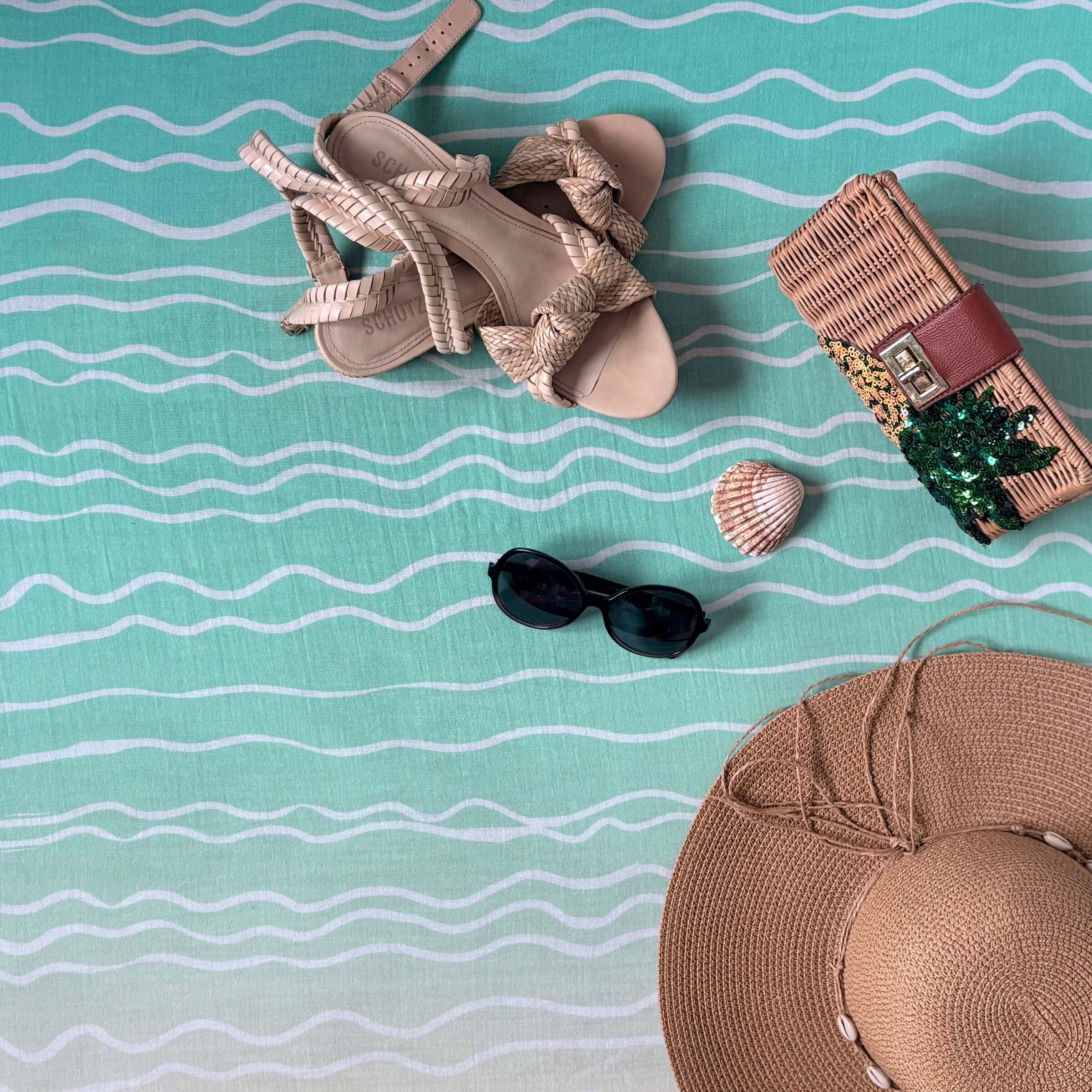Beige sandals, sunglasses, shell, and straw hat on the large square blanket in Brisa do Mar design