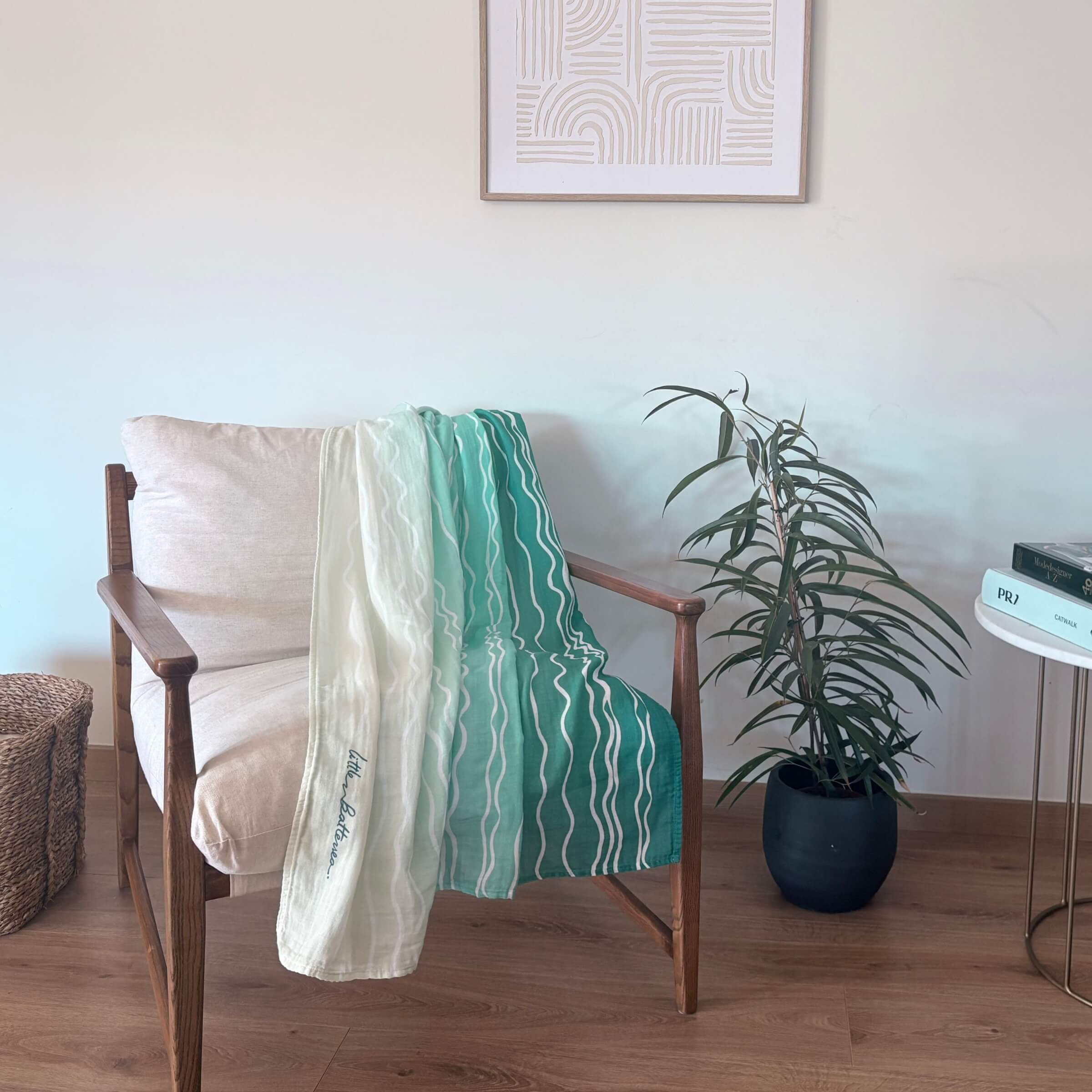 The Large Square Brisa do Mar as Sofa throw towel cotton blanket, draped over a modern wooden chair in a living room with a palm tree plant and framed picture on the wall.
