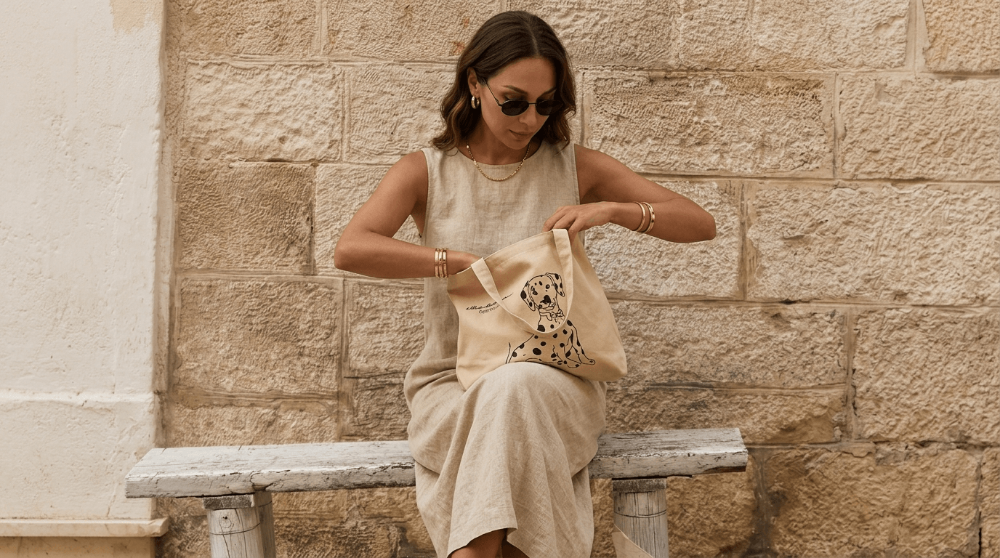 Woman sitting on a stone bench holding a tote bag against a stone wall.