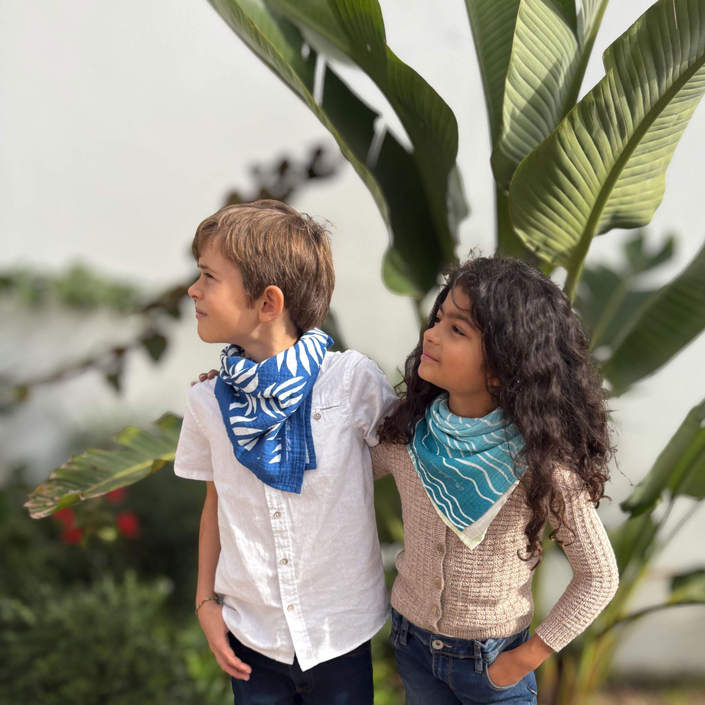 Two children wearing Small Square muslins outdoors, showing versatility and everyday wear beyond infancy.