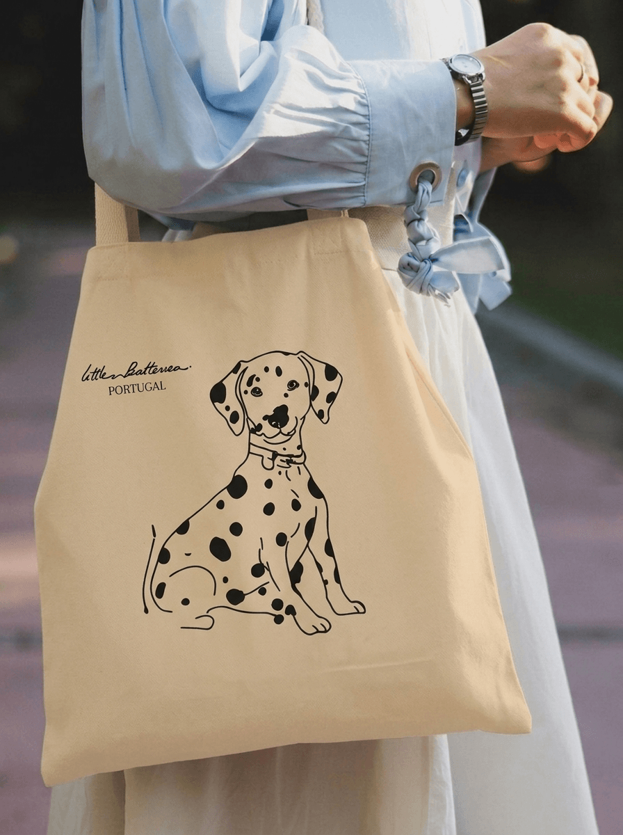 Beige tote bag with a black dog illustration held by a person wearing a light blue shirt.