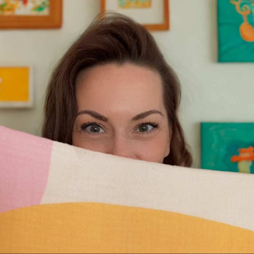 Woman peeking from behind a colorful pillow with abstract art in the background