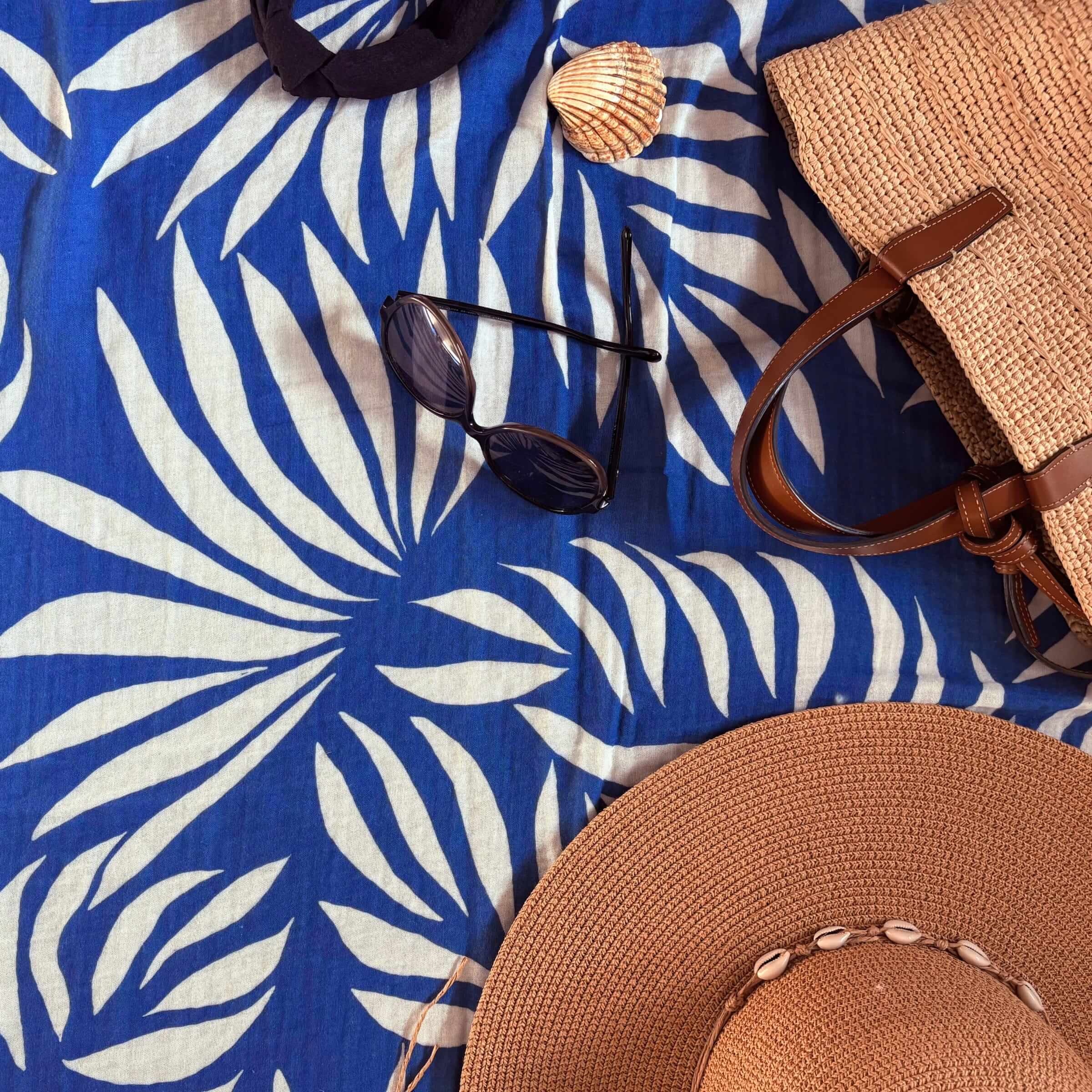 Blue leaf-patterned towel with sunglasses, shell, and straw bag on top