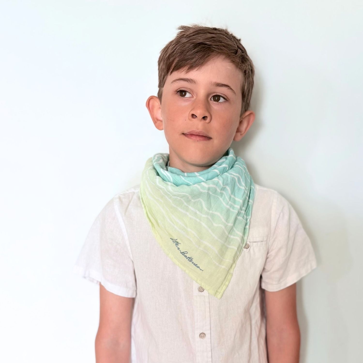 A boy wearing the Brisa do Mar Small Square muslin as a neck scarf, demonstrating continued use as the child grows.
