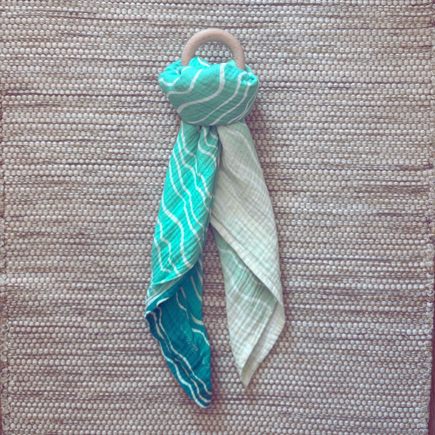The Small Square muslin tied in a knot around a baby teether, demonstrating versatility beyond swaddling, its also great for play.
