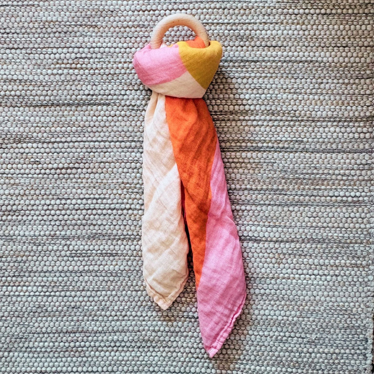 The Small Square muslin tied in a knot around a baby teether, demonstrating versatility beyond swaddling, its also great for play.