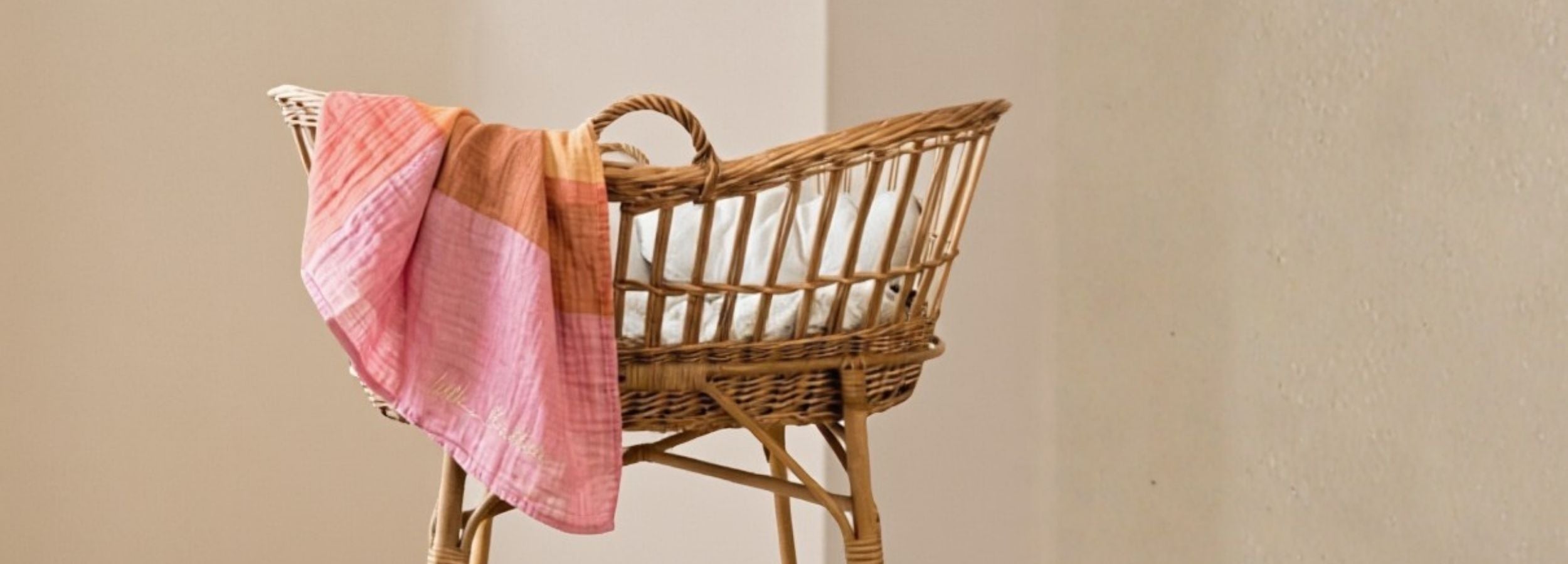 Wicker baby crib with pink and orange blanket against a beige wall
