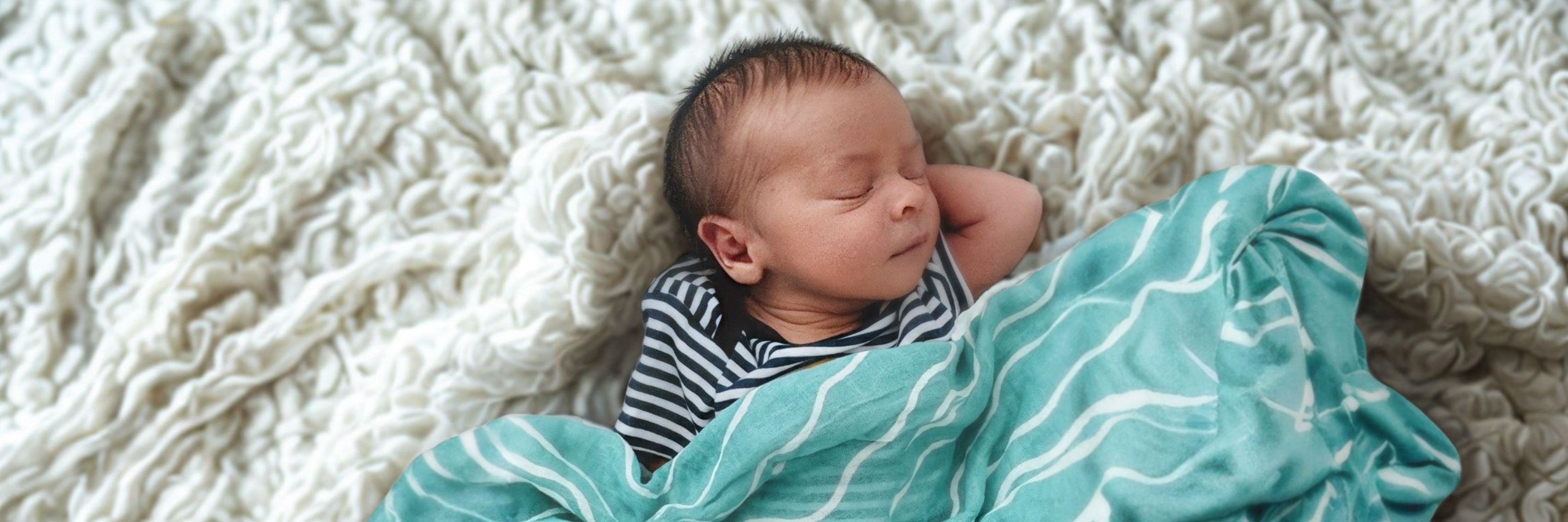 Newborn baby sleeping with a cosy muslin blanket 